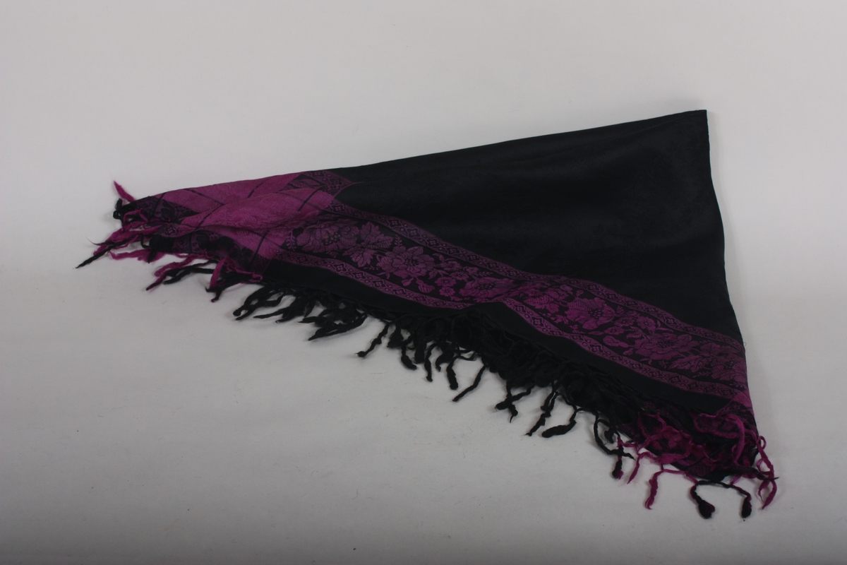 Heilmønstra silkeklut, hovuddelen svart med ruter med blomar,, som markering rundt eit breitt felt med sterkt fiolettte blomar. Om bruk, sjå litteraturrreferanse.
Frynser