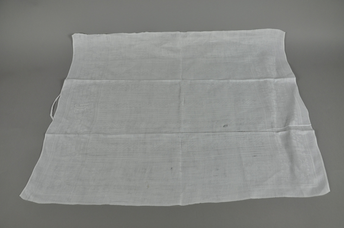 Hvitt håndkle av lin, rektangulær form. Tekstilen er noe slitt.