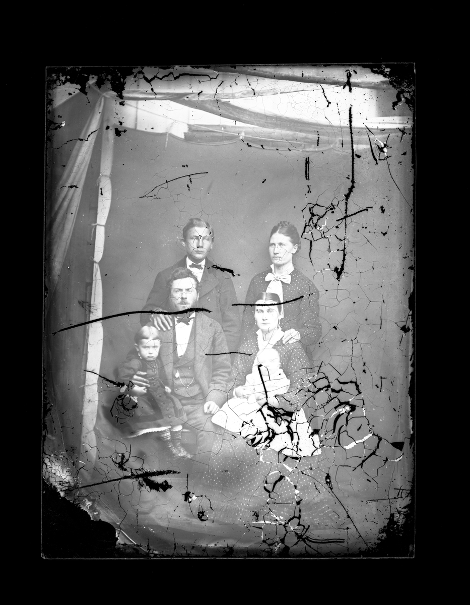 Fotosamling etter fotograf Knut Aslaksen Berdal. f. 1829 Einlaugdalen Vinje, d. 21.01.1895. Gruppeportrett. Mann og kvinne sittende med barn på fanget. Mann og kvinne stående bak.