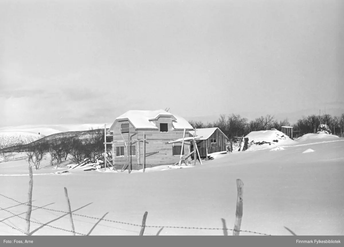 Et gjenreisningshus og et fjøs under oppbygging i Seida, februar-mars 1947. I "Gamle bilder fra Tana" sitt Facebook innlegg kan man lese at huset tilhørte til Isak Per Andersen. Og at dette er et av få gamle hus i Tana med valmet tak, dette er halv-valmet. Begge hus står igjen.
