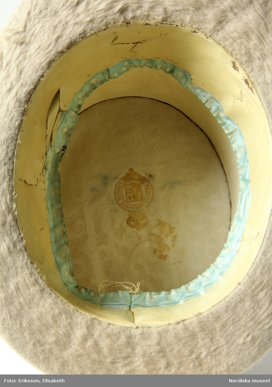 Cylinderhatt i beigefärgad silkesfelb med ripsband i samma färg. Tillverkad på 1850-talet av Christy & Co. Ltd., London.