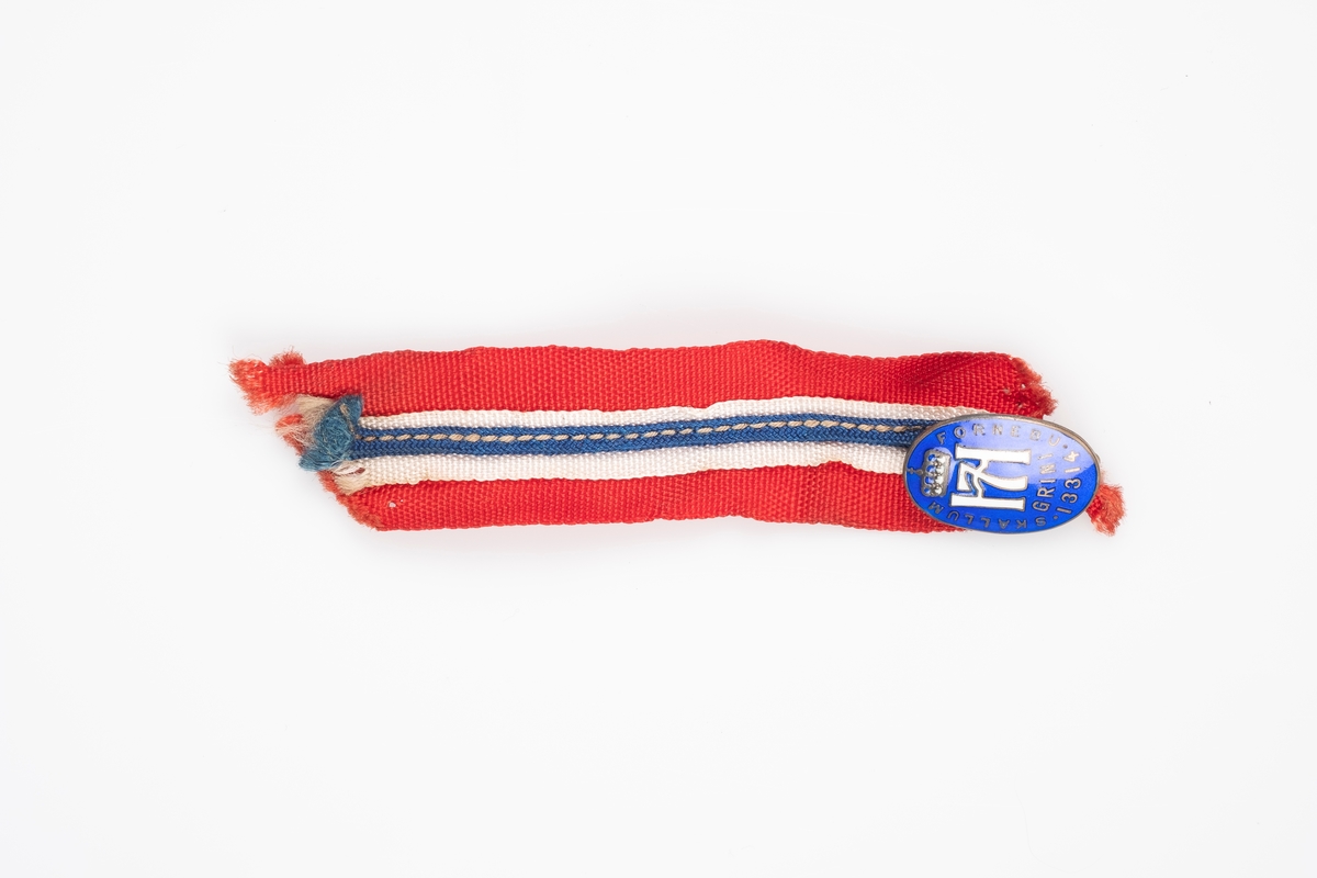 Et lite ovalt merke (nål) som er festet til et bånd med farger som symboliserer det norske flagget. Merket er blå med Haakon VII monogram