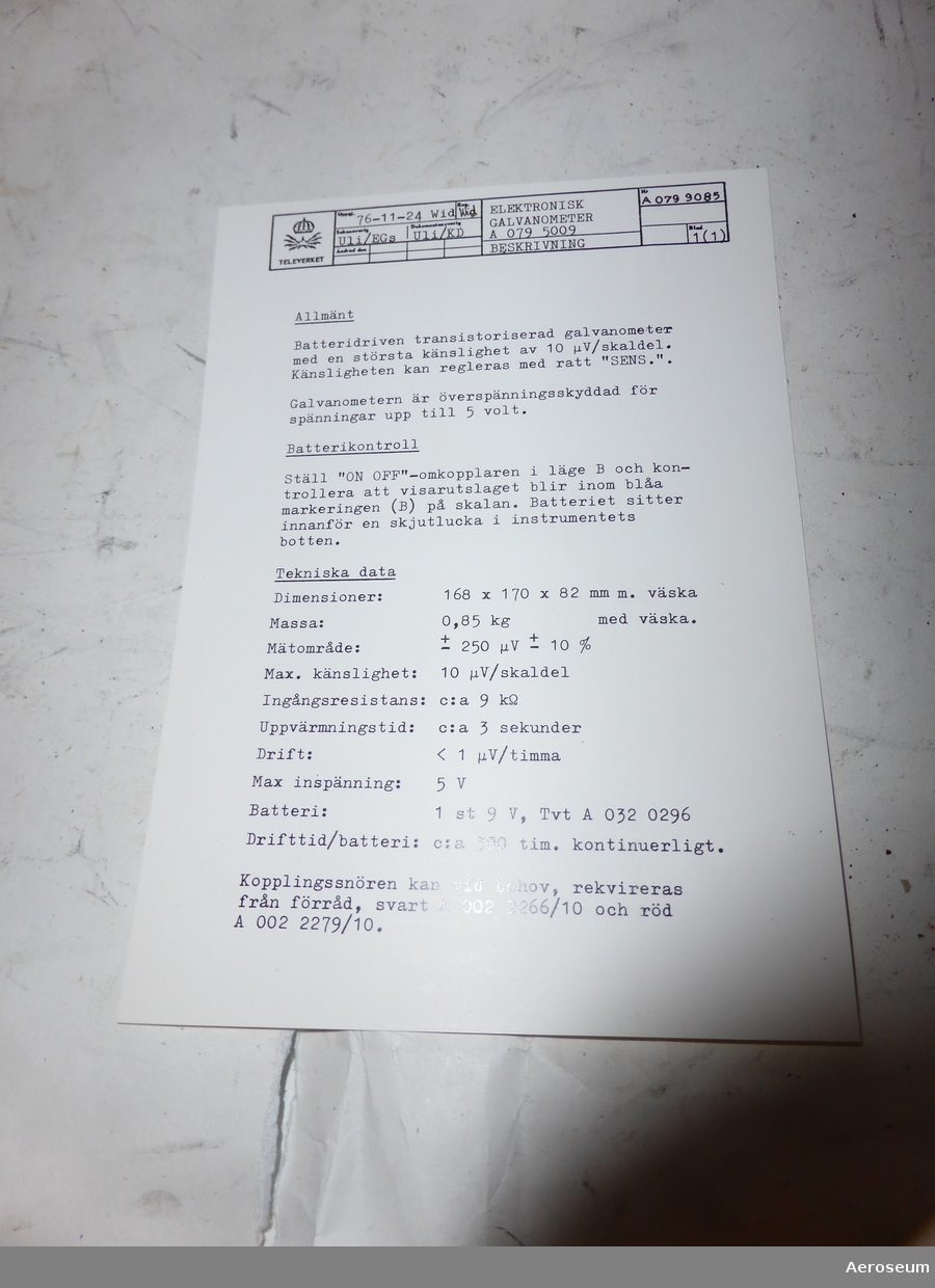 En galvanometer i en svart läderväska. I en plastficka som sitter fastsatt i väskans bärrem finns det en manual på engelska, en lapp med instruktioner på svenska, och en extra manual för en mätspänningskälla. Galvanometern är tillverkad av Yokogawa Electric Works, Ltd. i Japan.