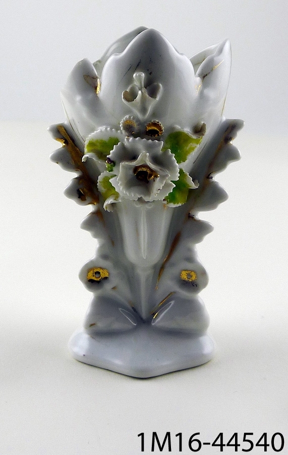 Vas, porslin, med blommor (varav troligen en nejlika) och blad på framsidan, detaljer målade i grönt och guld. Vasen är något skadad.