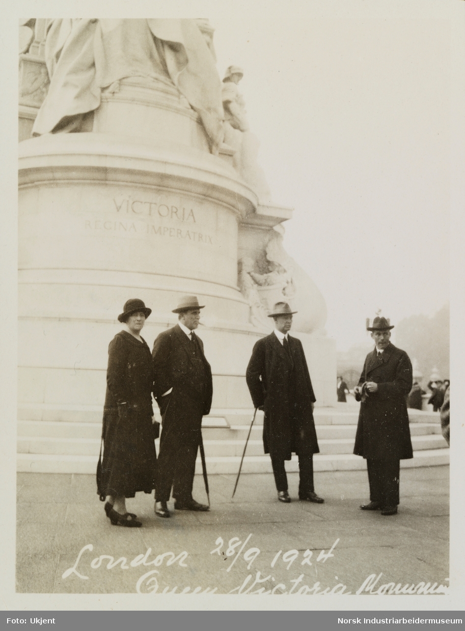 Tre menn og en kvinne står foran Dronning Victorias minnesmerke, Queen Victoria Memorial ved Buckingham Palace i London