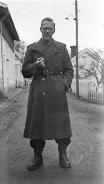 En man med glasögon, militär rock och en cigarett i handen står på Bergsgatans södra del utanför nr 6.
