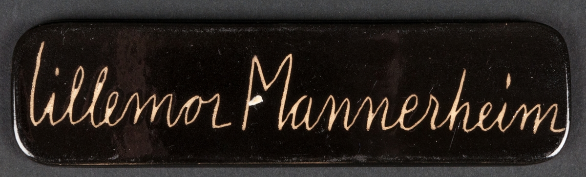 Skylt i svart med stämplad dekor, texten lyder: lillemor Mannerheim.