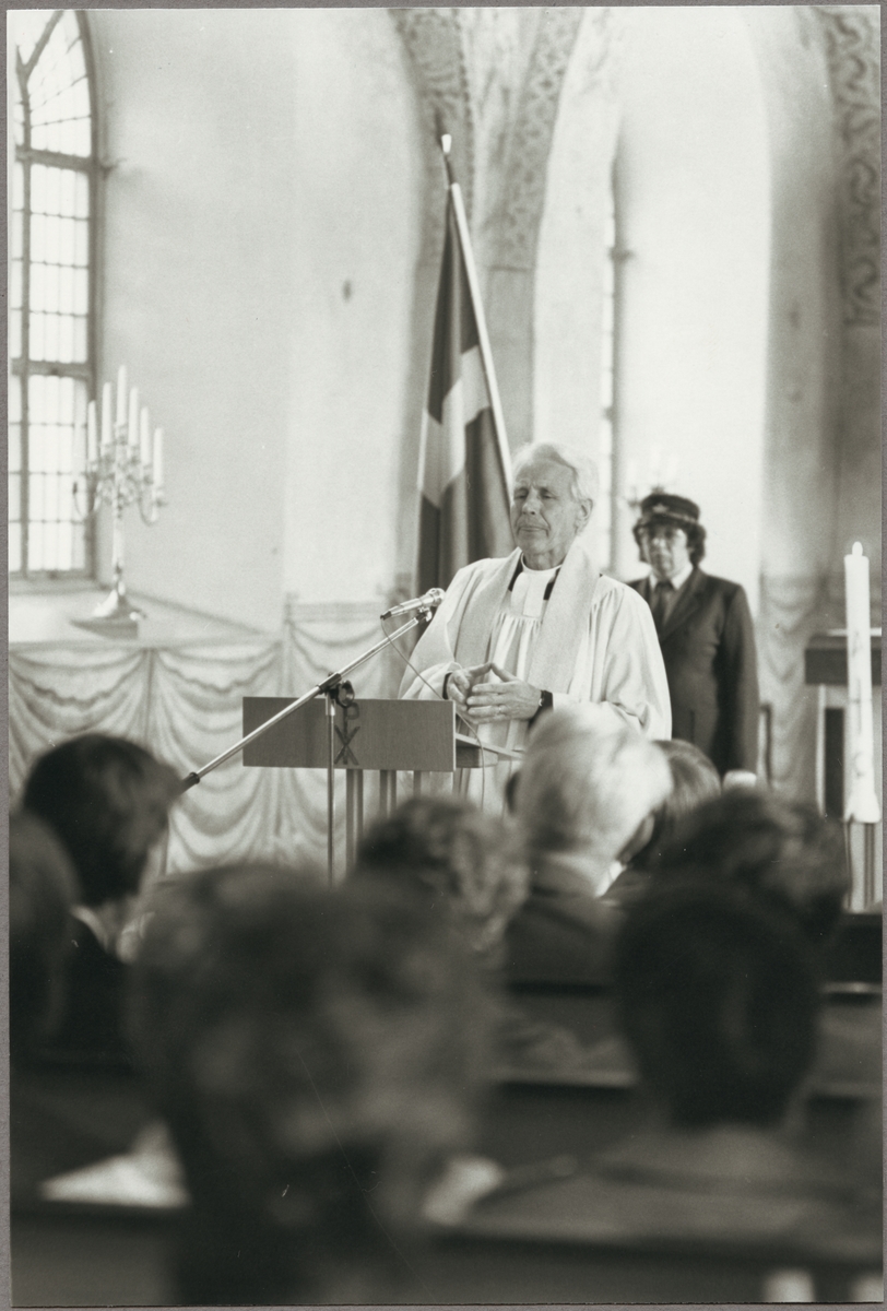 Kyrkoherde Lars Byström talar i Torshälla kyrka på Trafikaktiebolaget Grängesberg - Oxelösunds Järnvägar, TGOJ-dagen den 22 maj 1987. Fanbärare Ingeborg Jakobsson står i bakgrunden.