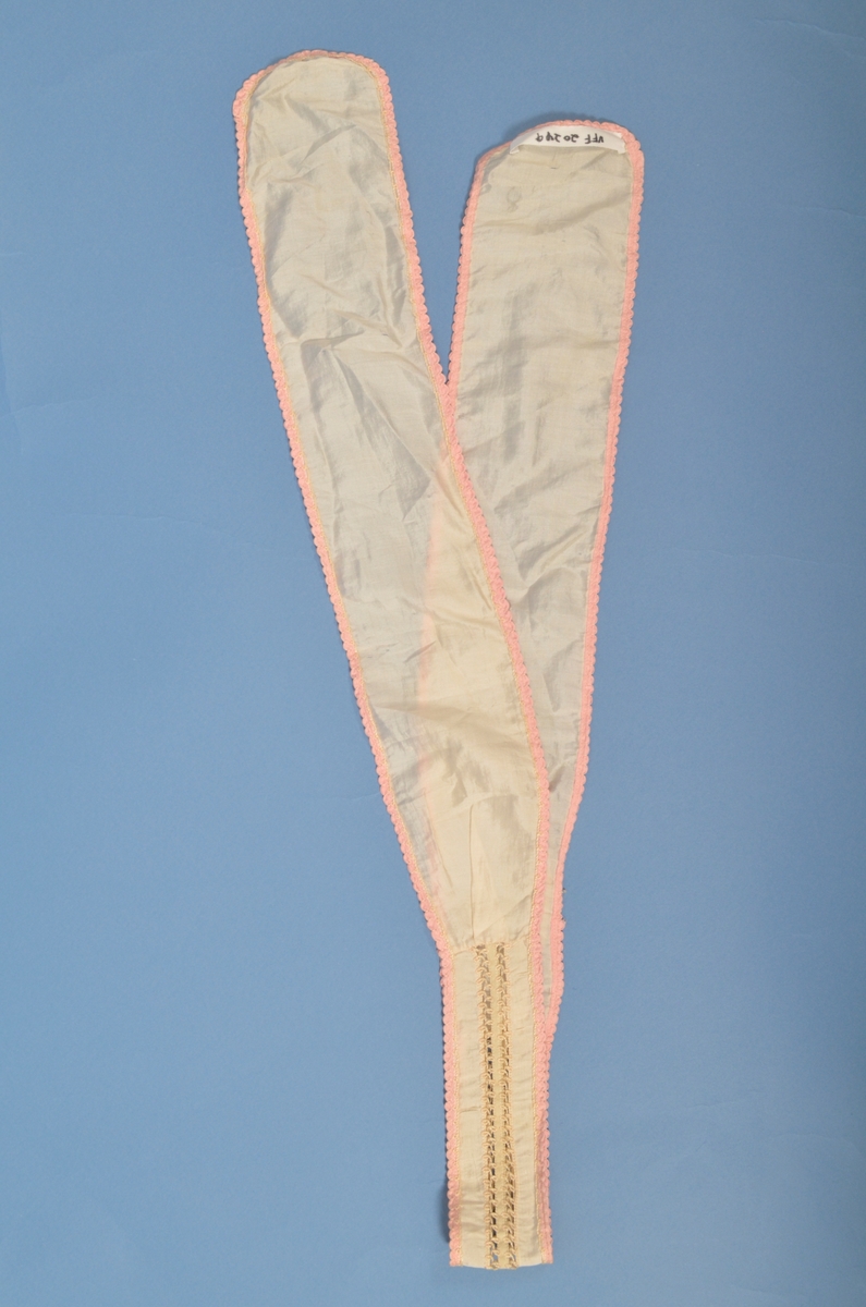 Halssløyfe i tynn kvit silke, kanta med rosa band. Midt på bandet pryda med band og kryssesting.