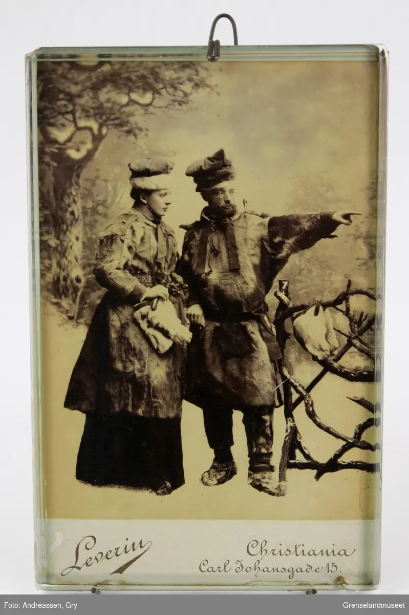 Studiefotografi av Distriktslege Andreas Bredal Wessel og hans kone Ellisif Wessel ikledd pesk, skaller og stjernelue foran et tregjerde.