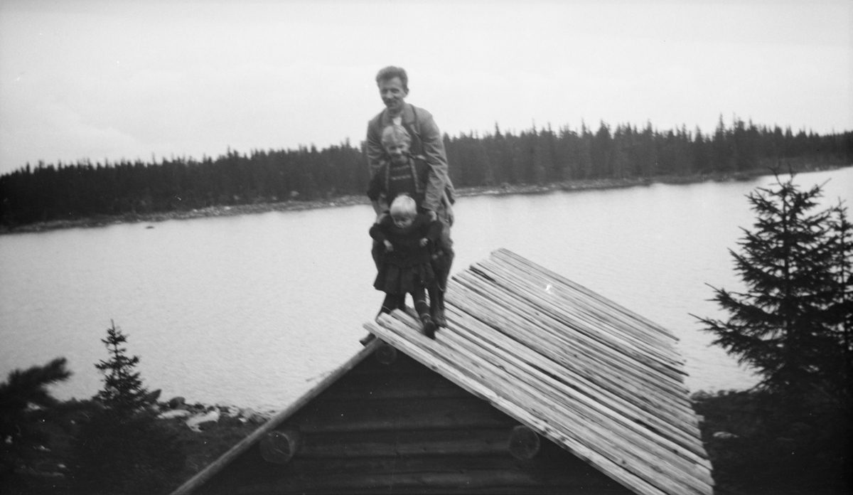 Mann og to barn stående på taket til ei fiskerbu eller et båtnaust