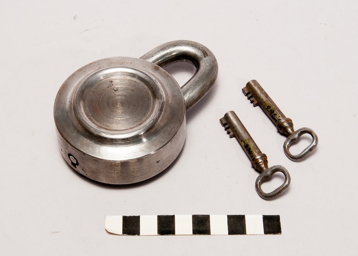 Hänglås av järn, jämte två nycklar. Etikett: "1 Patent Vorhänge Schloss, B 4". Stämpel: "K.K.A. Privl."