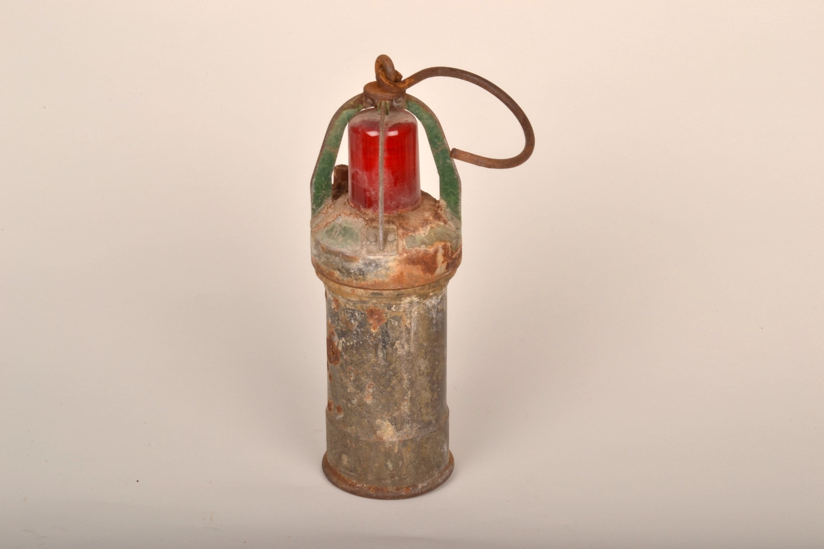 Sylinderformet lykt, med rød lampe på toppen. Lampen er metallbøyler. Stor krok er festet i toppen, til å henge opp lykta.