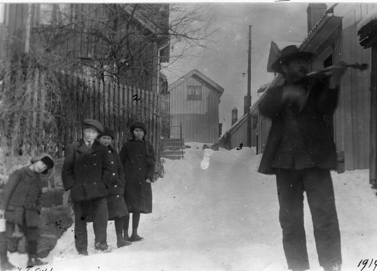 Parti fra Andølingen, ved øvre ende av "Prestebrua" utenfor Andresens snekkerverksted, (den gamle prestegården) barn og spillemann i gata, vinter. Kragerø