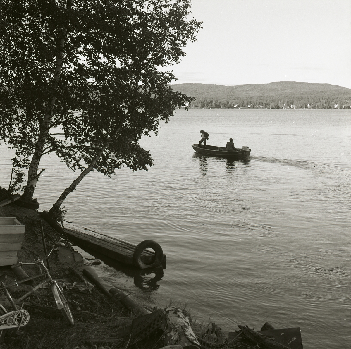 Två män åker i en motorbåt på sjön. I bakgrunden syns skog och berg, Ångermanland 1974.