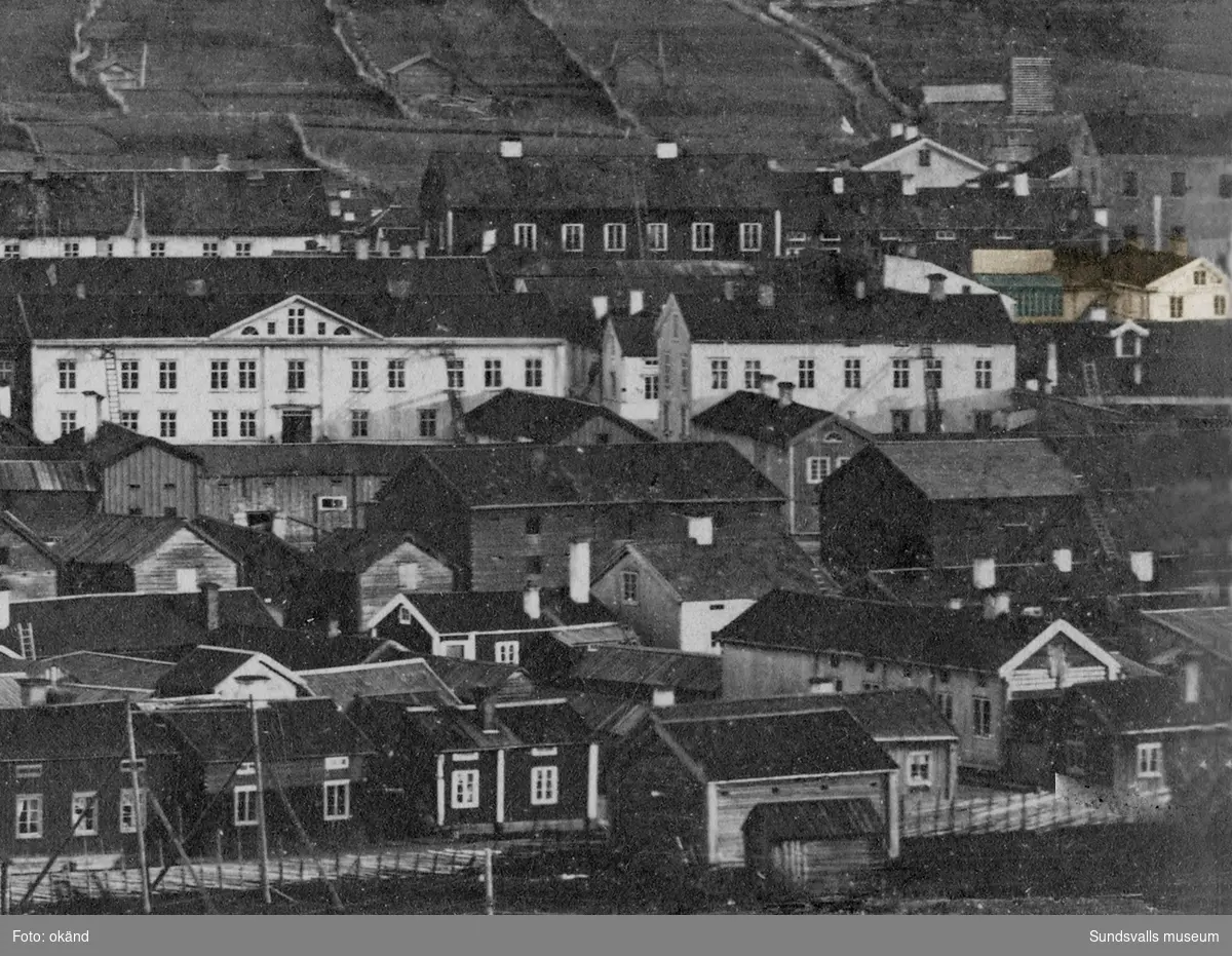 Vy över trästaden Sundsvall mot Södra berget. Bilden tagen före stadsbranden 1888. De två stora ljusa husen, till höger i bild, utmärker sig. Det vänstra ägdes vid denna tid av stadens då förmögnaste man, skeppsredaren och grosshandlaren Per Gustaf Dahlström f. 1807 d. 1883. Det högra huset ägdes av grosshandlaren August Sundberg f. 1824 d. 1900 (även far till författarinnan Maria Rieck-Mûller). Längst ut i högerkanten skymtar F W Hellbergs ateljé med ett stort ateljéfönster (färgad del se bild 2).