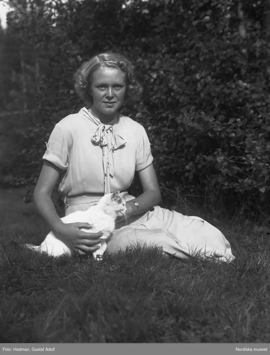 Ung kvinna sitter i gräset med en katt.