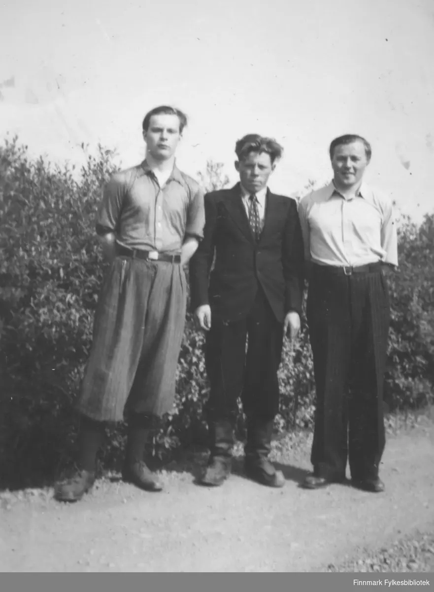 Tre unge menn står i veikanten med en hekk bak dem og poserer for fotografen. De er fra venstre: Erik Andersen, Mathis Mathisen og Aslak Eliassen. Stedet er ukjent.