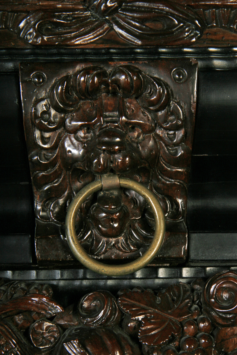 Jakaranda (?) finér, ibenholt, to dører med fyllinger og tre glatte søyler i fronten, skuff nedentil metallring i gesimsen.