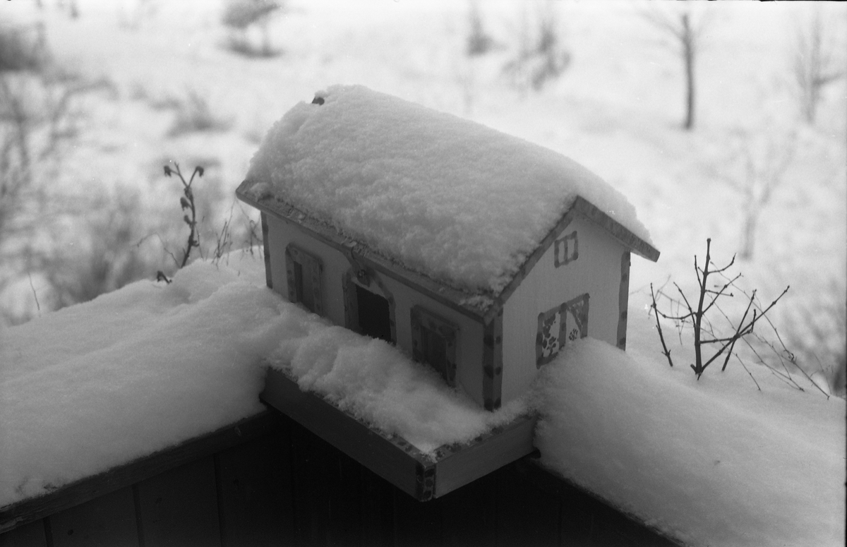 Fuglebrett utformet som miniatyrhus. Vintermotiv.