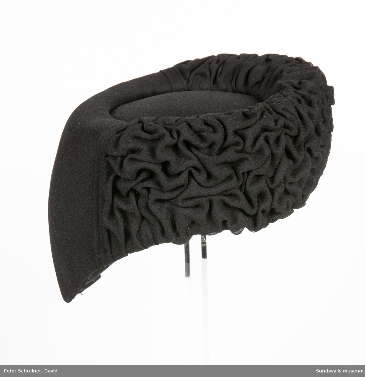 En svart hatt med neddraget nackparti, stoppad slät kullplatta och framkant i murkelstrukur.