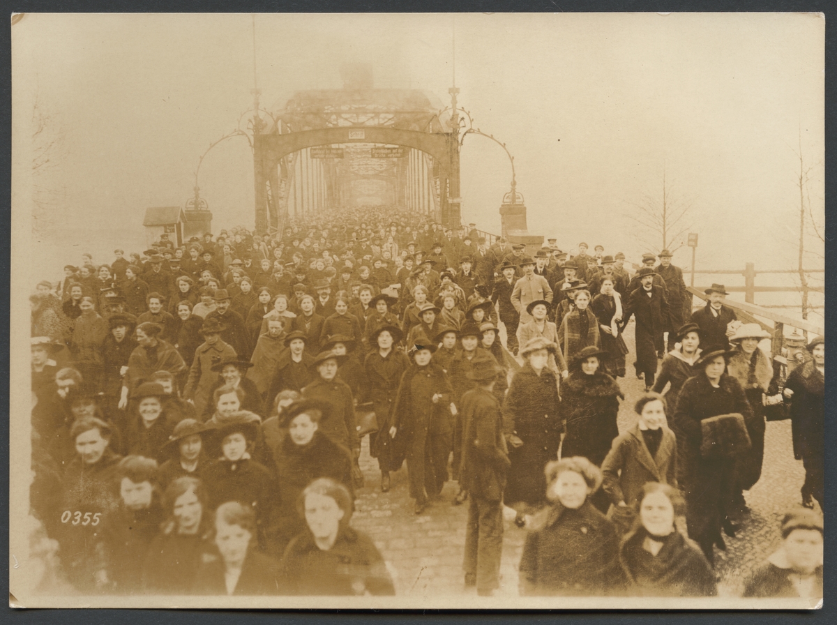 Bilden visar en folkmängd som består övervägande av kvinnor som rör sig över en bro, som syns i bakgrunden, rakt emot fotografen.