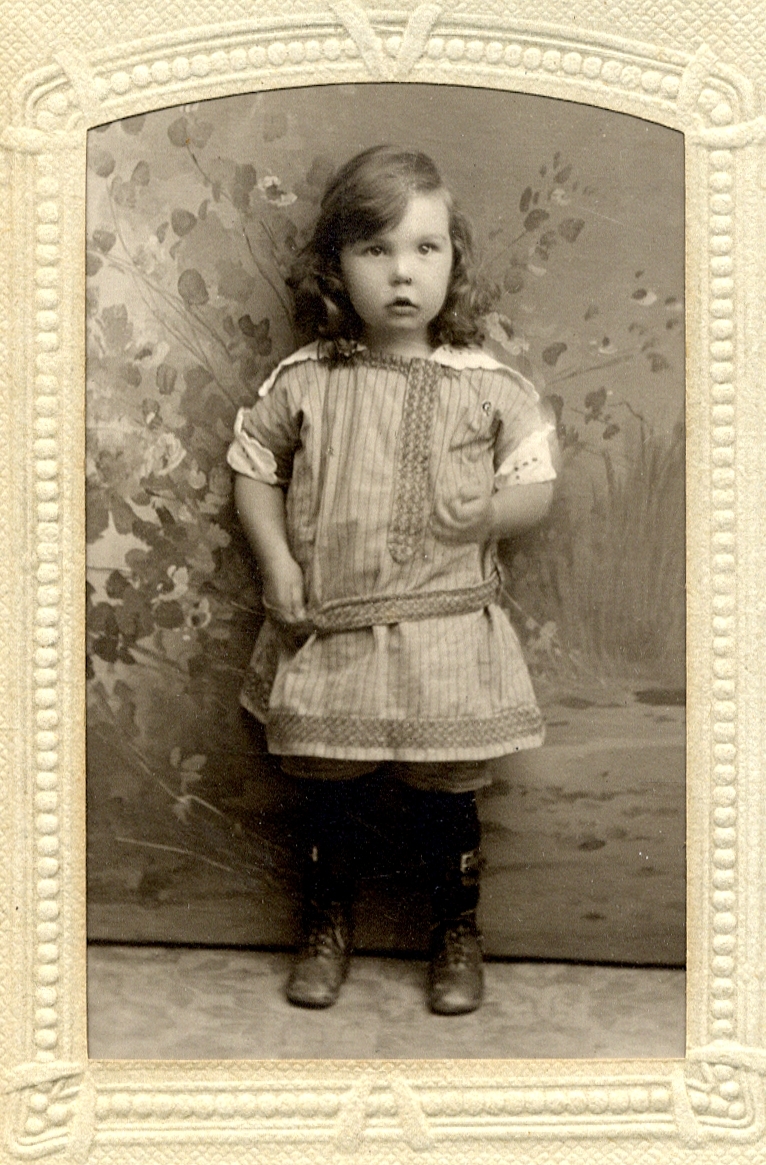 Foto av en liten flicka* i koltliknande klänning. 
Helfigur. Ateljéfoto.

*Kan möjligen vara: Blenda Ingeborg Maria Slycke (1915-2012), f. i Rappestad, Östergötland.