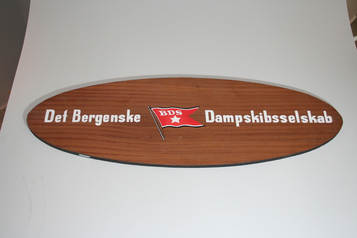 Skiltet er ovalt  med navnet til rederiet Det Bergenske Dampskibsselskab med tilhørende rederiflagg i midten. Bokstavene er hvite. Skiltet er likt på begge sider.