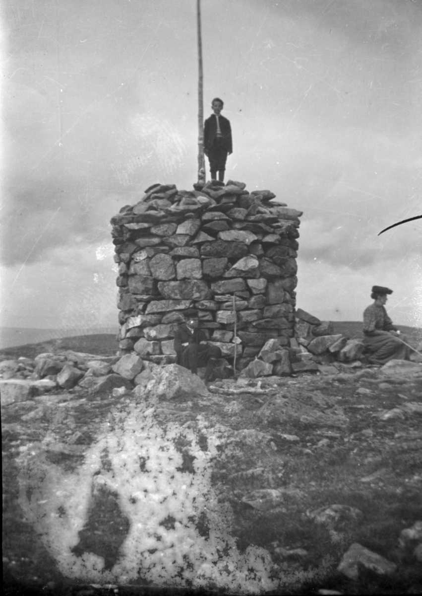 Familie ved en varde på en fjelltopp; gutten har klatret opp på varden