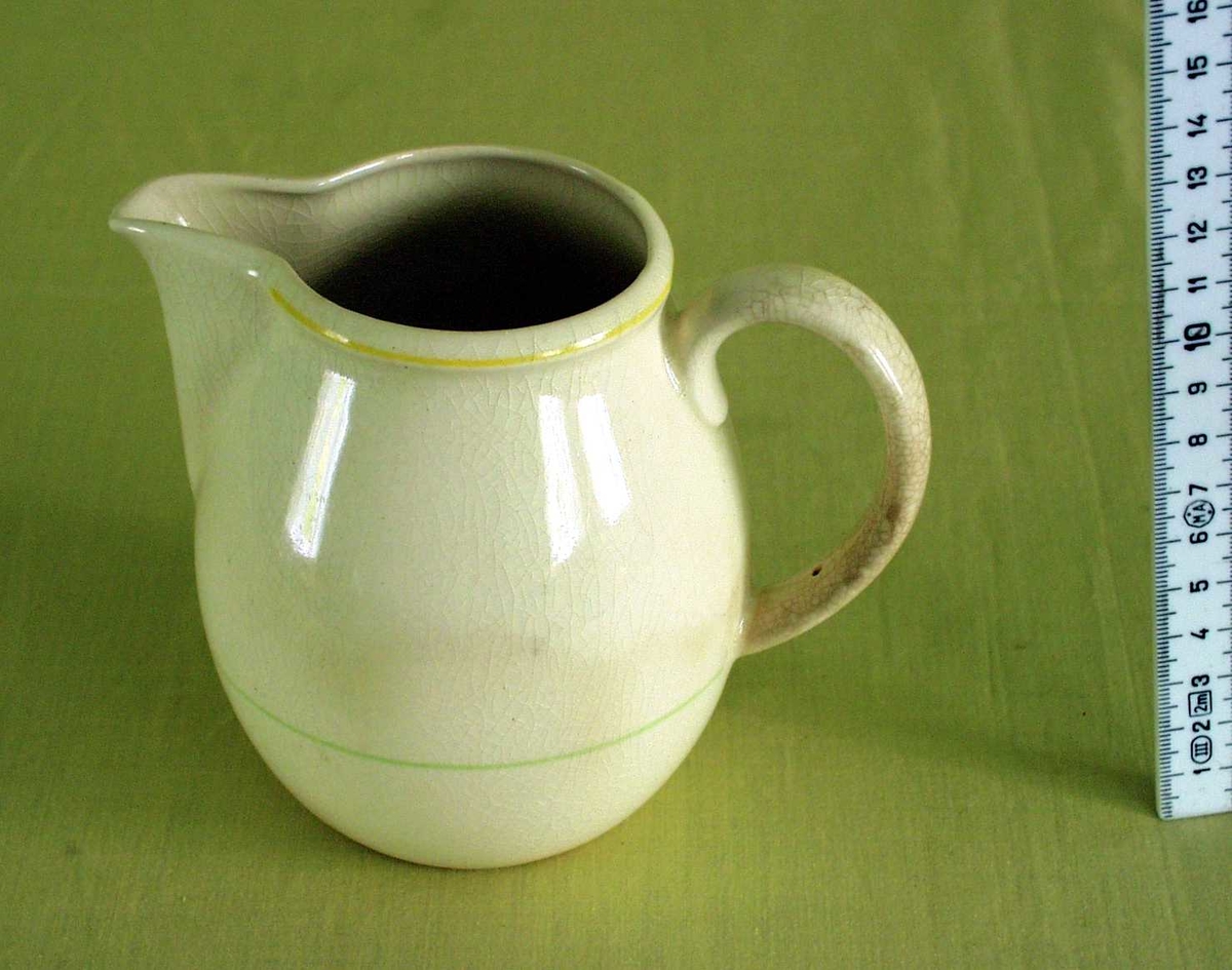 Hvit, keramisk mugge. Til servering av melk. 
Tynn, gul dekorativ strek rundt halsen på mugga, og tynn, lys grønn strek på nedre del av mugga.
