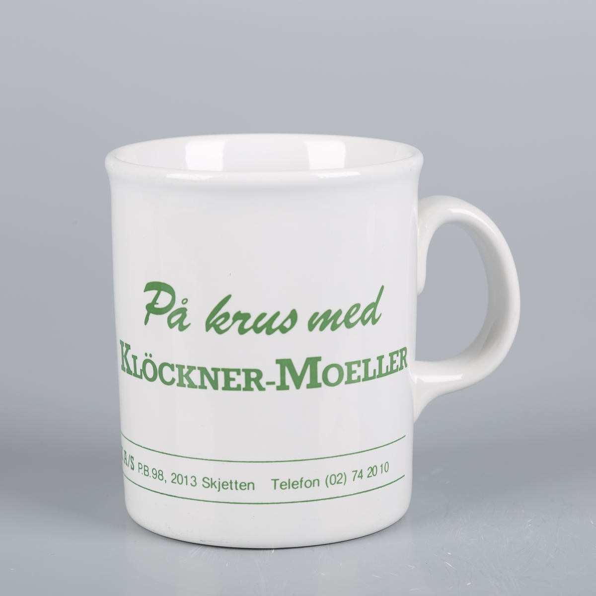 Krus med hank. Klöchner-Moeller-logo. To avisutklipp er vedlagt, med informasjon om flyttingen av bedriften Klöckner-Moeller fra Aurskog-Høland til Skedsmo.
