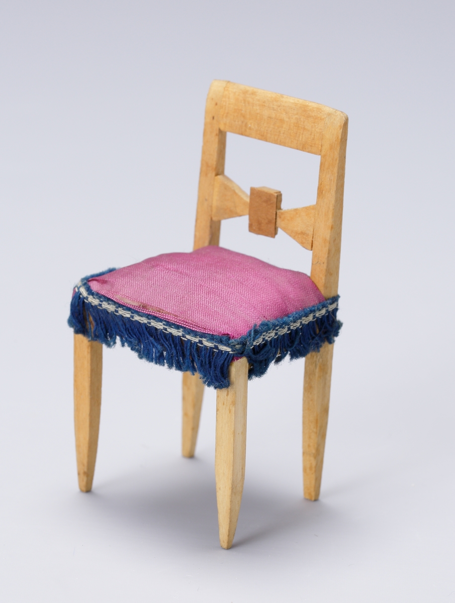 Dockskåpsmöblemang av furuträ bestående av fem stolar, en soffa och ett bord, klädda med lila siden. Runt kanterna band och frans av blått bomullsgarn. Bordet svarvat.

Inskrivet i huvudkatalog 1938.