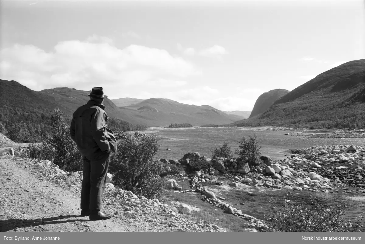 Olav Lien med hatt og hendene i lomma på Skutebui med utstyn mot fjellet Vinjekyrkja