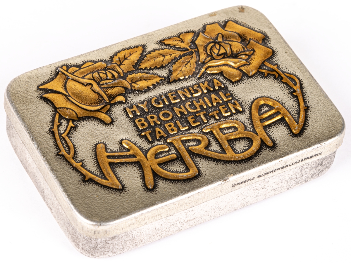 Tablettask i plåt, silverfärgad botten med rosdekor och text i guld: "HYGIENISKA BRONCHIALTABLETTEN HERBA".