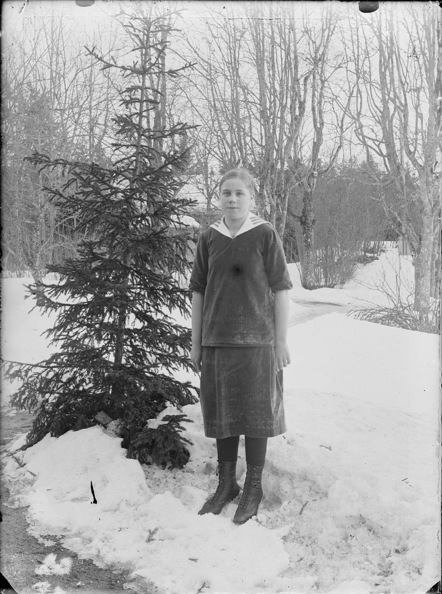Flicka står vid en gran i snön, Alunda, Uppland