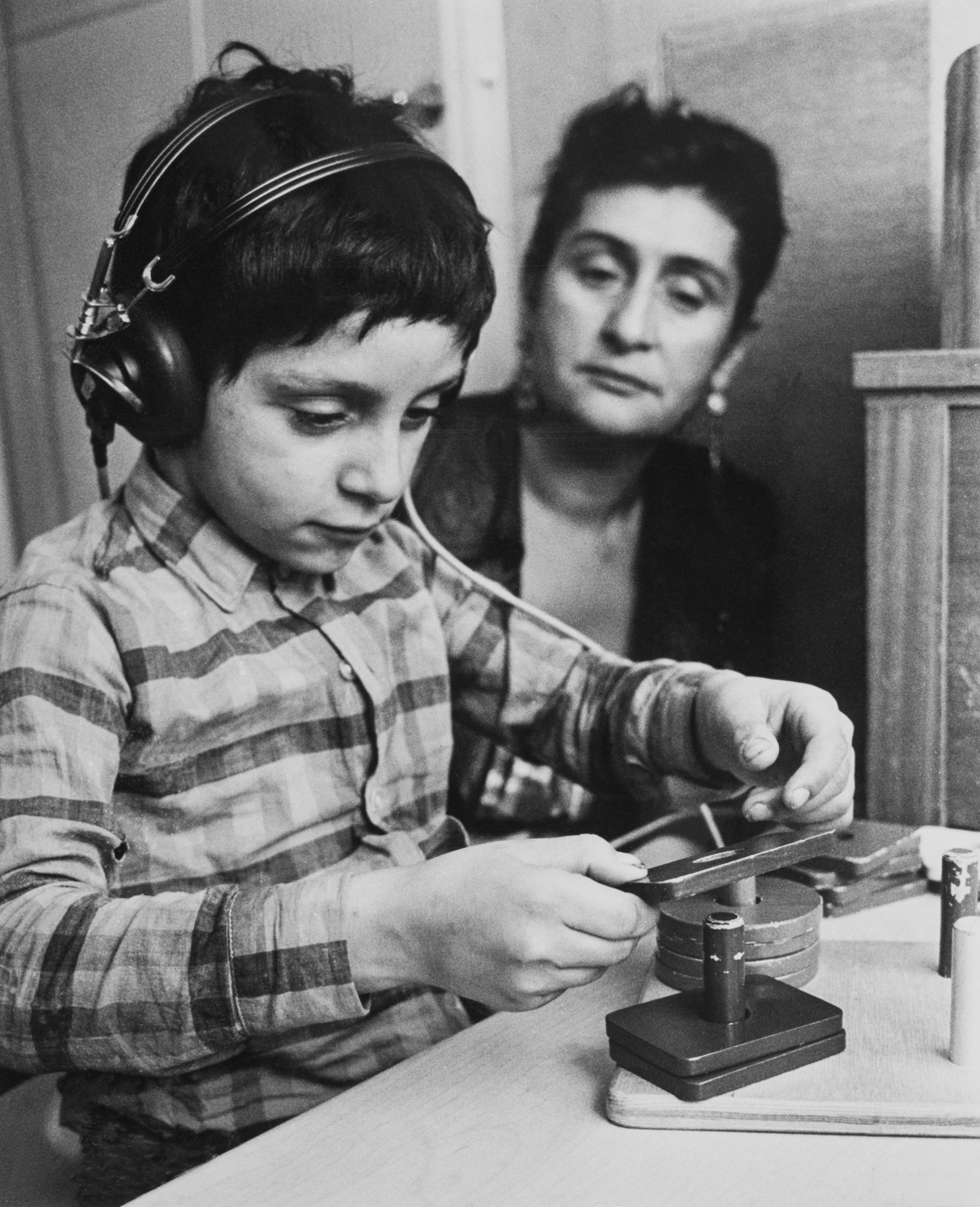 En pojke får för första gången besöka en riktig hörselklinik. Han har hörlurar på öronen och lägger en ring över en pinne.