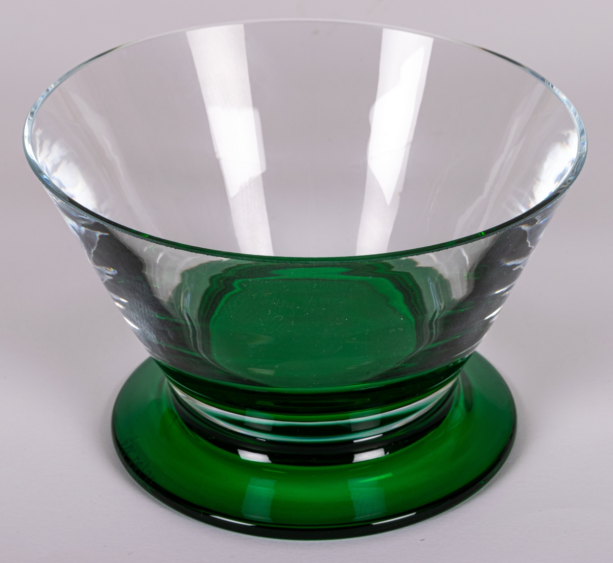 Skål. Raka, utåtlutande sidor i ofärgat glas på låg, utkragad fot i grönt glas. Design Gunnar Cyrén för Orrefors Glasbruk.