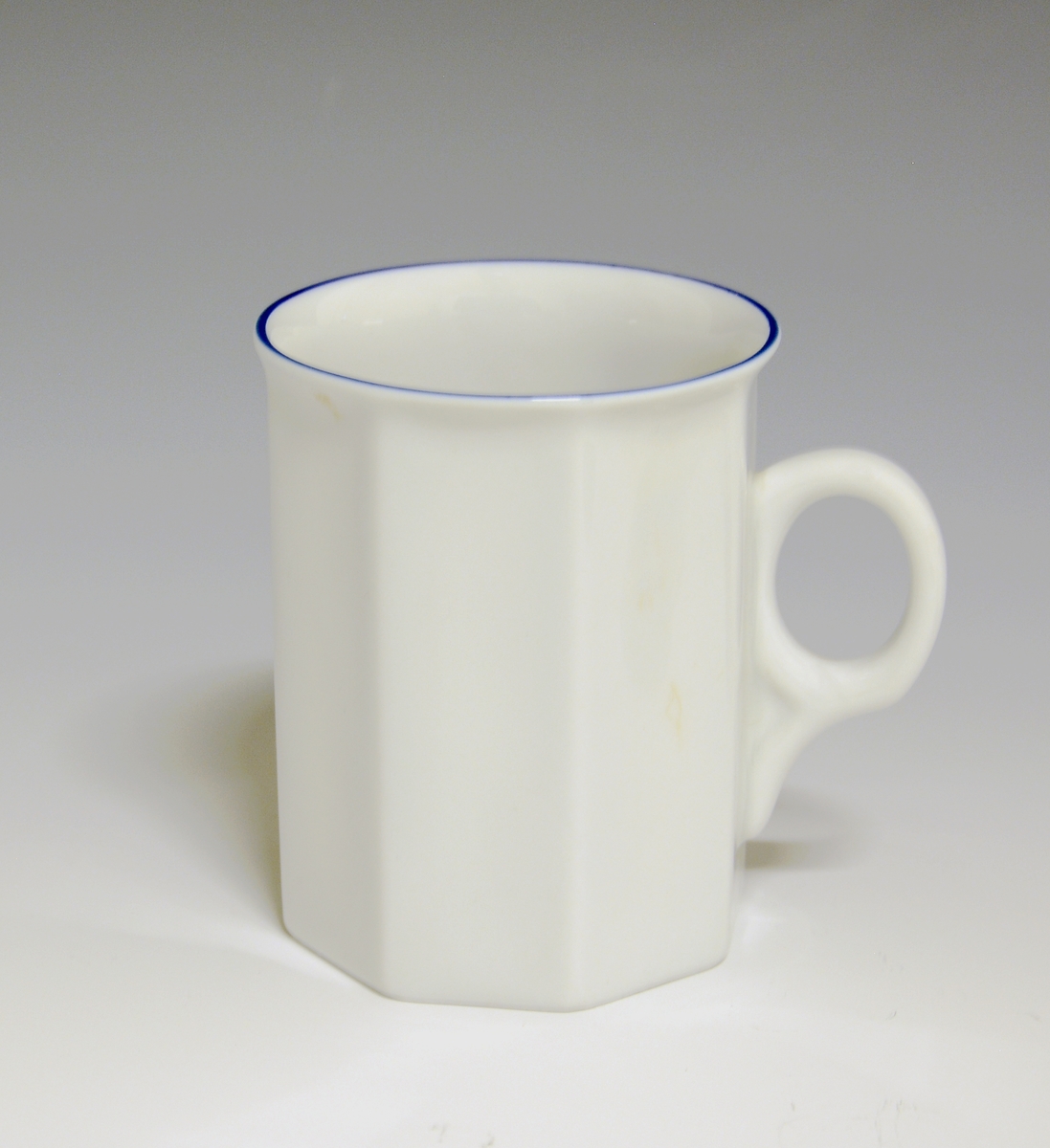 Mangekantet kopp i porselen med blå kantstrek som eneste dekor. Hvit glasur.
Modell: Octavia, tegnet av Grete Rønning i 1977.
Dekor: Blå strek