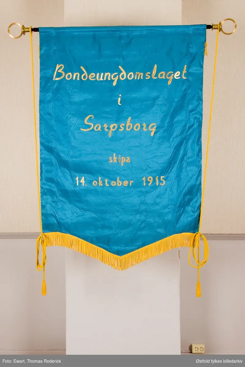 Fane  til BUL Bondeungdomslaget i Sarpsborg, stiftet 14.oktober 1915. Forside.
Tekst på bakside:
Bondeungdomslaget i Sarpsborg skipa 14. oktober 1915.