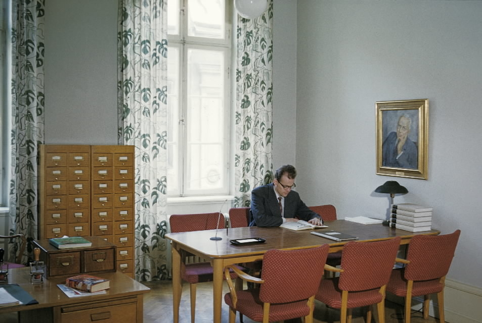 Bild 33 i en serie av 38. Bibliotekets läsrum, med fönster mot
Lilla Nygatan. Som besökare agerar museets vaktmästare postiljon Nils
Svensson.