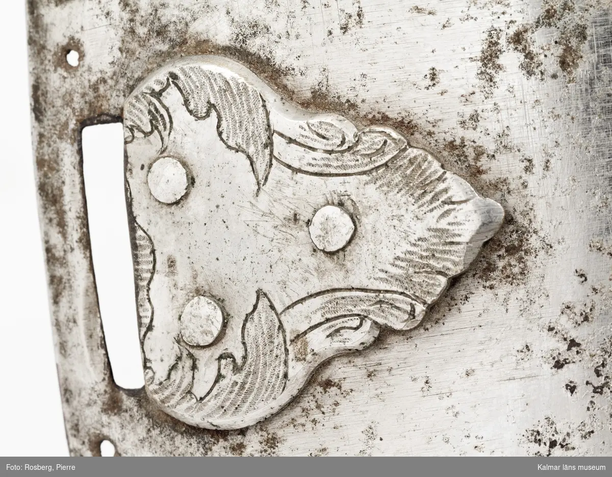 KLM 14814:1-2 Harnesk med jourbricka. Av bleckplåt. Med graverade rembeslag av silver. I de omvikta kanterna hål för fastsättande av foder. Framtill och upptill sex hål för fastsättande av någon dekoration (krönt riksvapen eller liknande, enligt huvudliggaren ska det vara en jourbricka med Gustaf III:s skiffer).