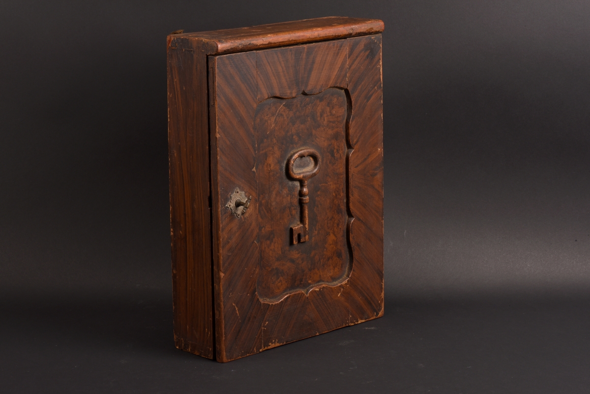 Rektangulärt nyckelskåp med vänsterhängd dörr av furu. På skåpsdörren är det en utsnidad nyckel. Skåpets utsida är målat i brun marmorering. Inne i skåpet tre böjda metalltenar för att hänga nycklarna på.