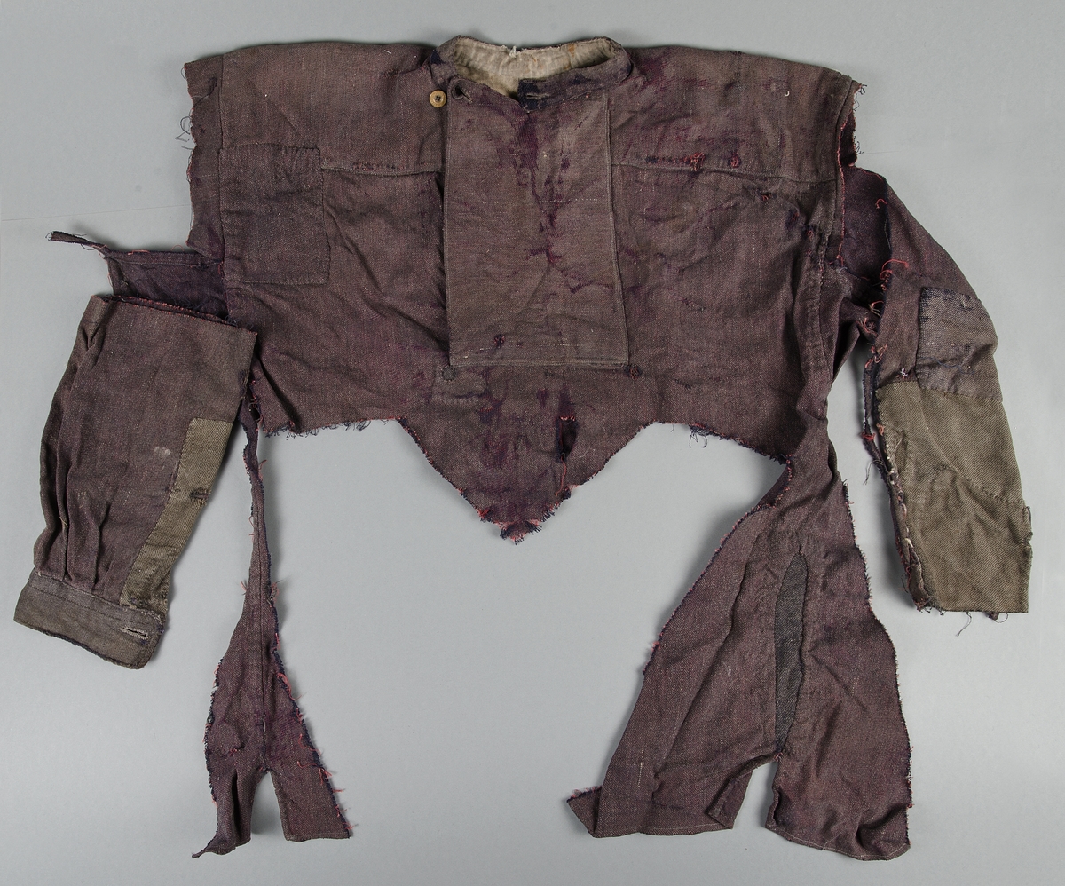 Två fragment av herrskjorta med bröstdel, krage, sidor med sprund, samt del av ärm bevarade i en del. Murarkrage, två olika kanppar.

En separat del med manschett och del av ärm. Ärmen lappad.