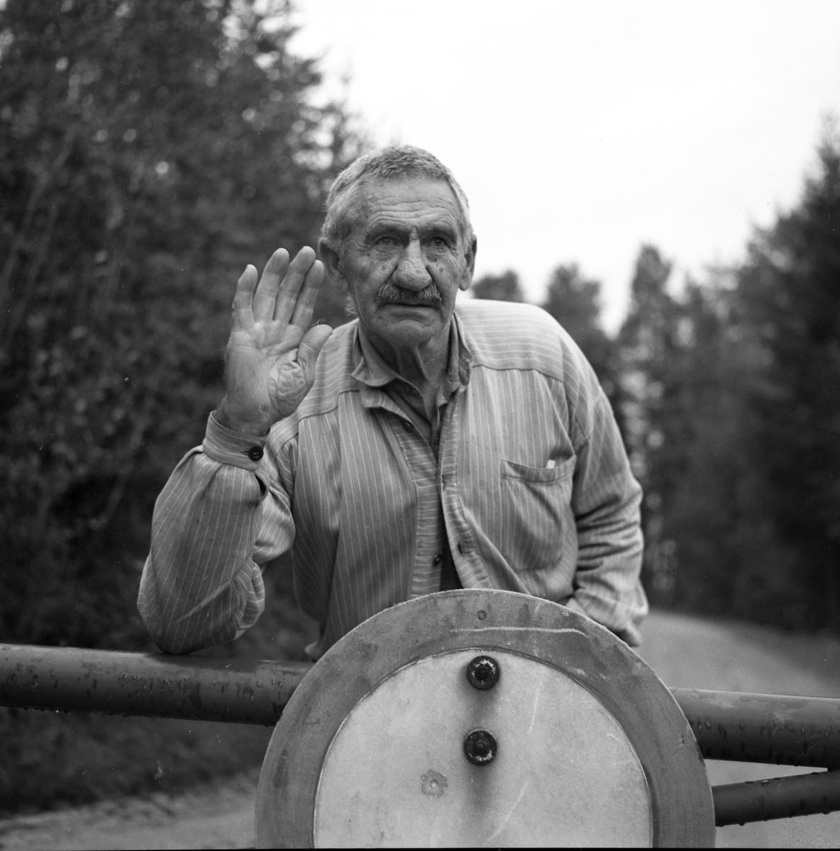 Anton Grønstad holder opp hånda, stående bak en bom ved en grusvei.