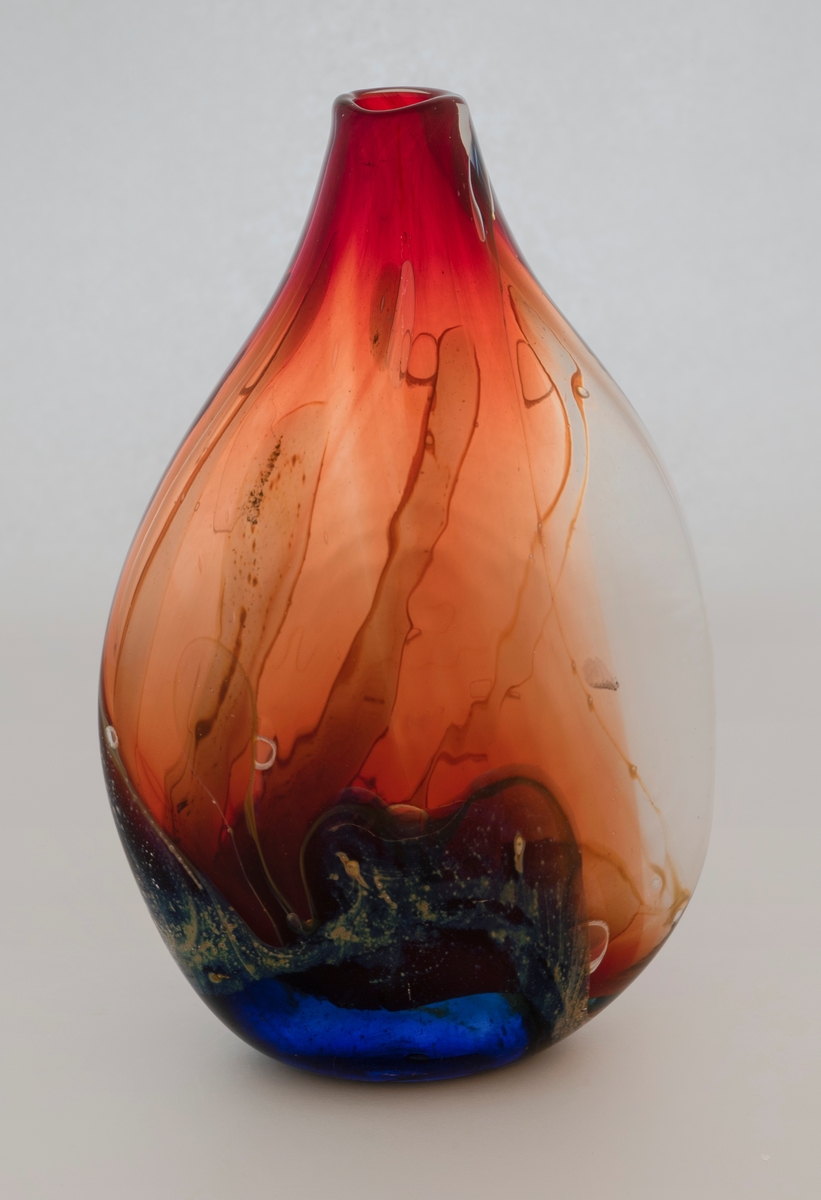 Flattrykket dråpeformet vase av farget glass. Korpus er rødbrunt med glidende fargeskiftninger i blått, hvitt og grønt. En del luftblærer i glassmasssen.