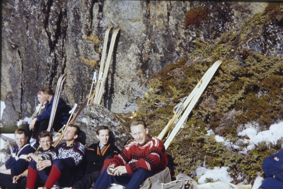 Folk på skitur soler seg foran en bergvegg.