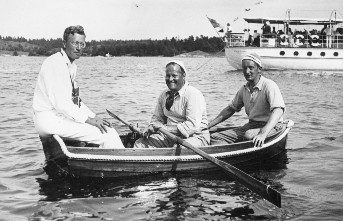 Tre män i en båt under KSSS:s långfärdssegling genom Södermanlands och Östergötlands skärgårdar i juli 1932. I mitten Gunnar Rooth, i aktern David Öhman, i fören oidentifierad person, i bakgrunden Erik Åkerlunds motoryacht STELLA MARINA.