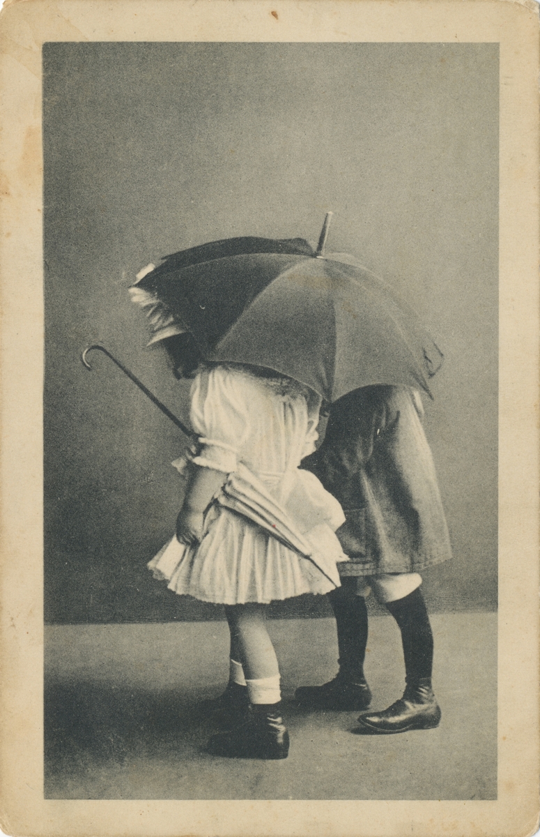 Postkortmotiv av to barn under en paraply.