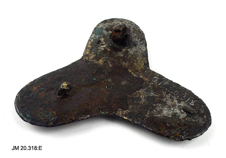 Treflikigt spänne av brons från 900-talet i Borrestil. Armarna, från centrum räknat, är 47 mm långa, 32 mm breda. Nålhållare bevarad men inte nålen. Textilrester kvar.