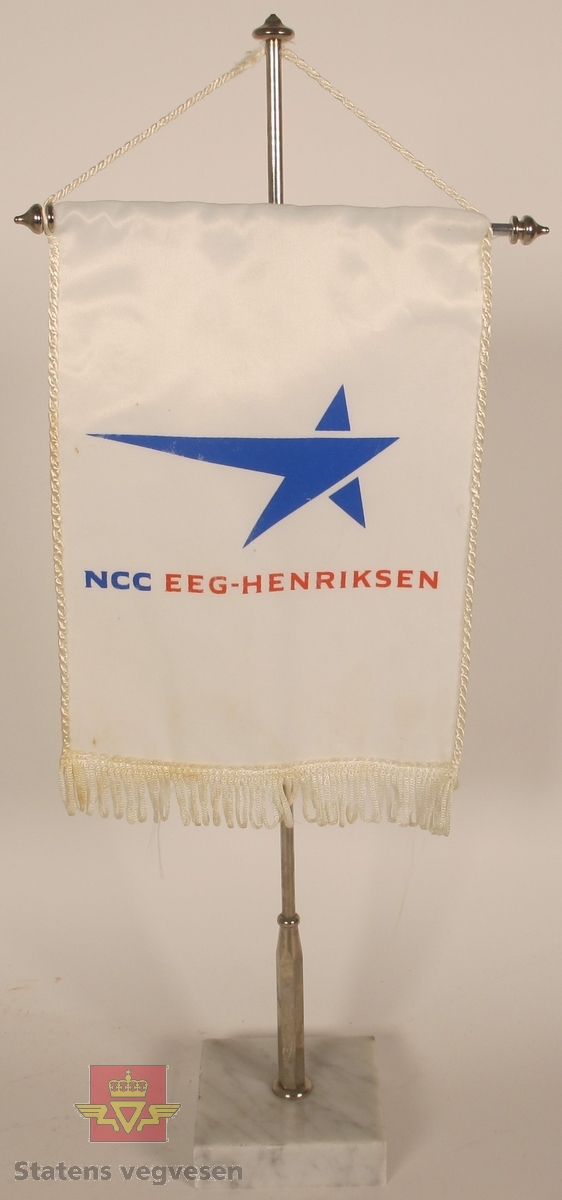 Bordvimpel med marmorfot, metallstenger og hvit vimpel i silke. Har påskriften NCC EEG-HENRIKSEN med NCC i blått og EEG-HENRIKSEN i rødt og en blå logo.